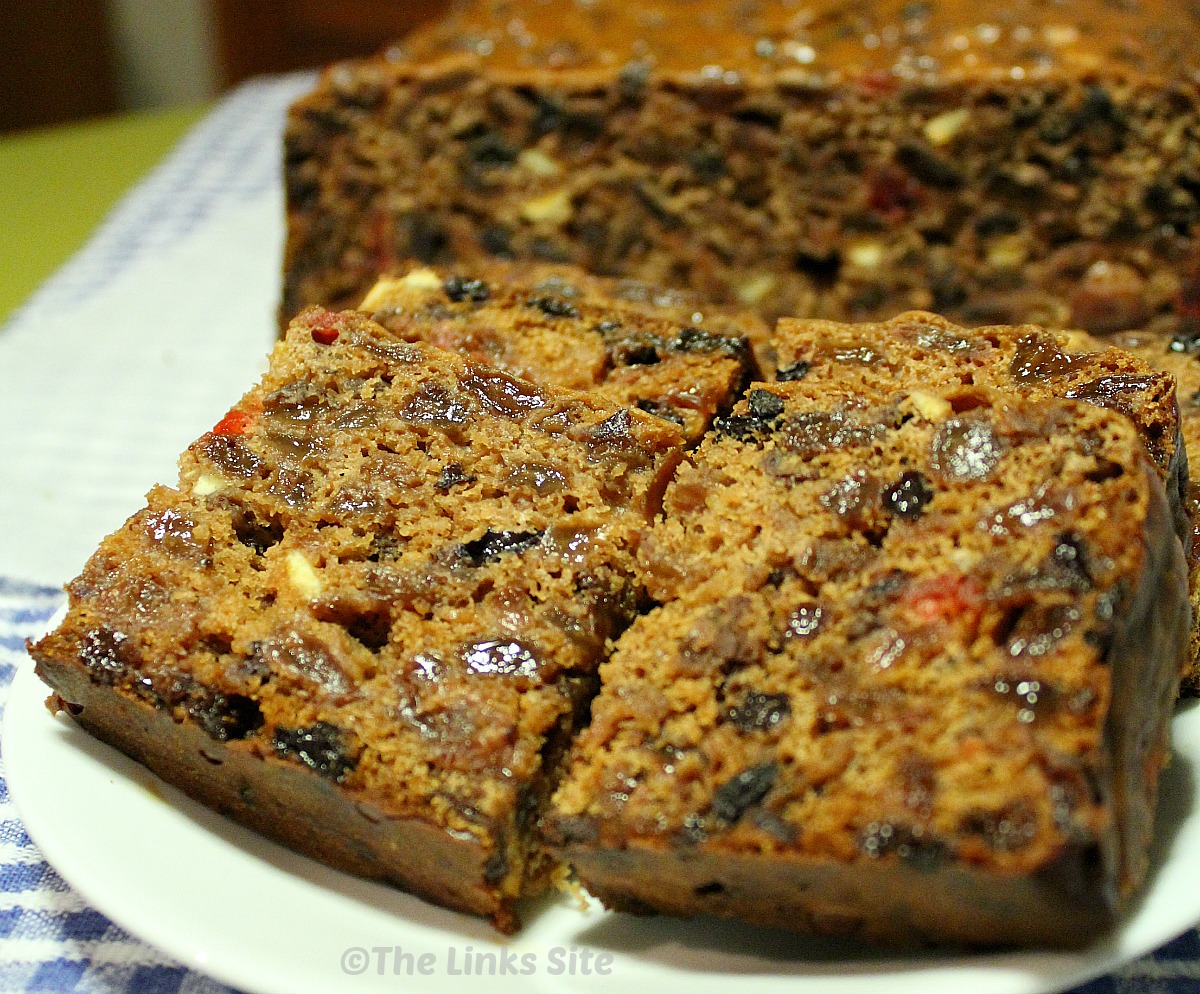 A white plate with pieces of fruit cake and the uncut portion of cake in the background.