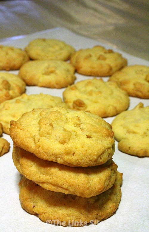 Stack of three cookies on baking paper, more cookies can be seen in the background.