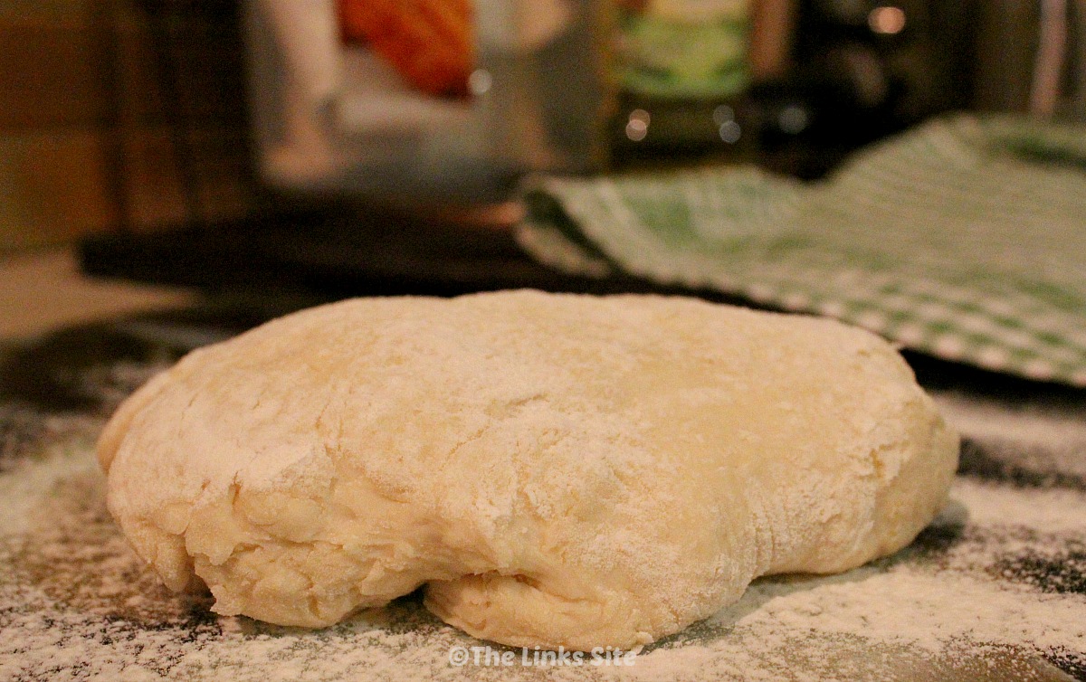 Ball of pizza dough dusted with flour on a glass cutting board. An olive oil bottle, flour packet, and tea towel can be seen in the background.