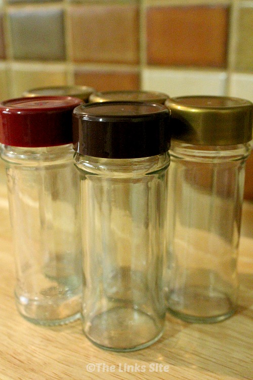 5 Empty glass spice jars with plastic lids pictured on a wooden cutting board.