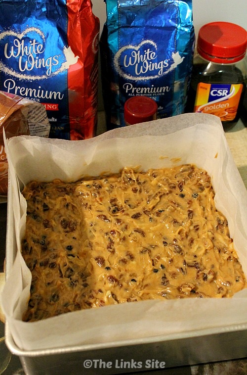 Christmas cake mixture in a square tin ready to be baked. Baking ingredients such as flour, sugar, and spices can be also seen.