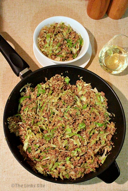 Overhead view of a fry pan containing chow mein. A white bowl of chow mein, as well as a glass of white wine, is placed next to the fry pan.