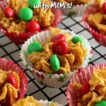 Honey Joys in Christmas themed paper cases on a wire cooling rack. Text overlay says: Crunchy Nut Honey Joys with M&M's!