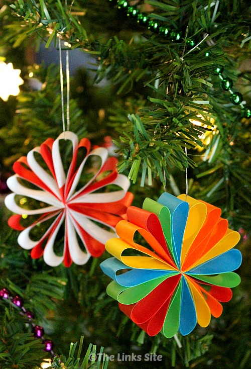 Two colourful paper decorations hanging from a Christmas tree.