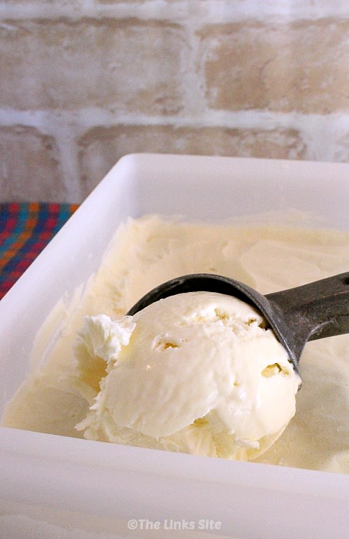 Plastic tub containing vanilla ice cream and a metal ice cream scoop is scooping up some of the ice cream.