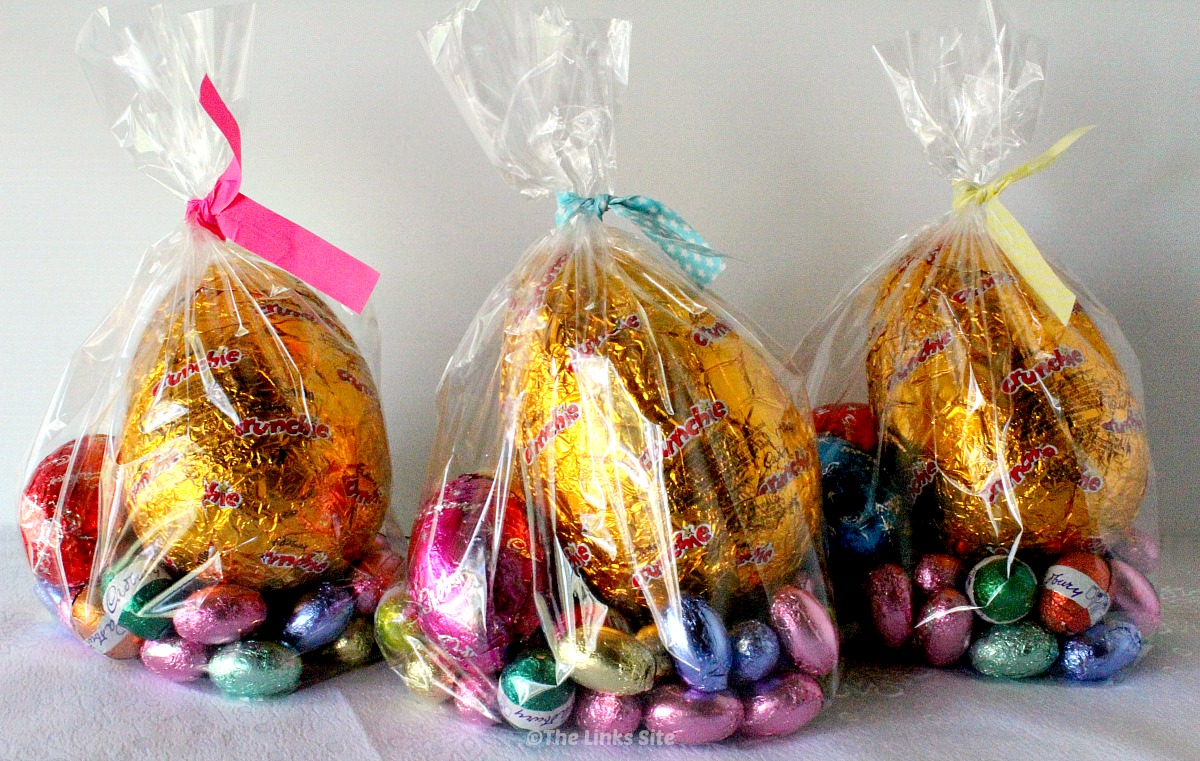 Three clear cellophane gift bags filled with various sized Easter eggs. The bags are fastened with Easter coloured twist ties.