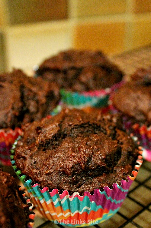 Chocolate muffins in multi-coloured paper cases sitting on a black cooling rack.