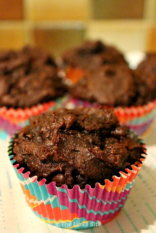 Close up of a chocolate muffin in a multi-coloured muffin case. Several other muffins can be seen in the background.