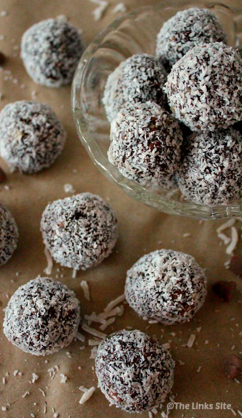 Walnut raisin balls arranged on brown paper. Several balls are placed directly on the paper with shredded coconut littered around them. The upper right of the photo shows some of the balls in a glass bowl.