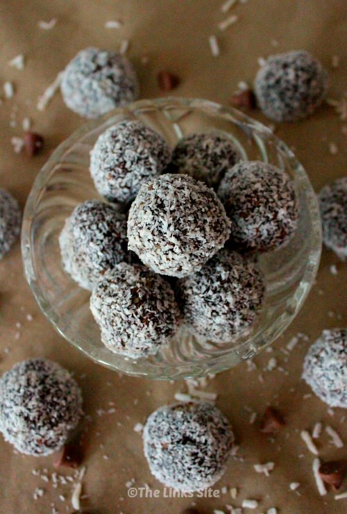 Overhead view of several walnut raisin balls in a glass bowl. Several other balls are spaced out around the bowl with coconut and chocolate chips also scattered around.