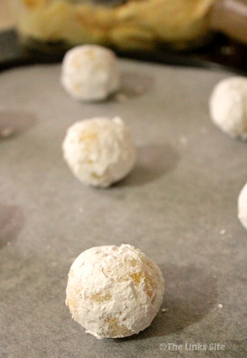 Balls of sugar coated cookie dough arranged for baking on a baking tray.