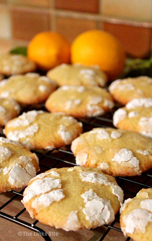 Lemon crinkle cookies on a cooling rack with two lemons in the background.