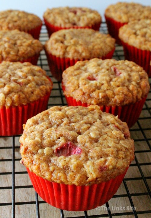 Several strawberry oat muffins in red paper cases sitting on black cooling rack.