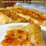 Slice of puff pastry quiche on a white plate. More slices of quiche and a tea towel can be seen in the background. Text overlay says: Ham & Cheese Puff Pastry Quiche (great for breakfast, as an appetizer, or as a main!).