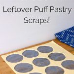 Leftovers from a sheet of puff pastry where circles have been cut from the sheet. The leftover pastry is lying on a wooden chopping board with a tea towel in the background. Text overlay says: What to Do With Leftover Puff Pastry Scraps!