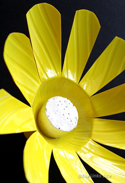 Close up of a plastic bottle flower that has been painted yellow. A wine cork that has been painted white is used to form the centre of the flower.