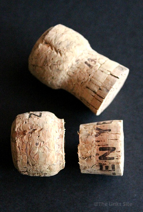 Two sparkling wine bottle corks on a black background. One of the corks has been cut in half.