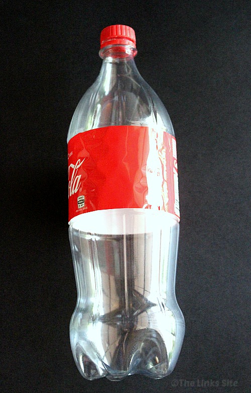 Empty plastic 1.25 litre Coke bottle lying down on a black background.