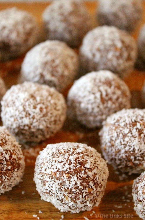 Coconut coated Yum Yum Ball are arranged on a wooden board. One central ball is in focus in the foreground and several other balls can be seen to the side and in the background.