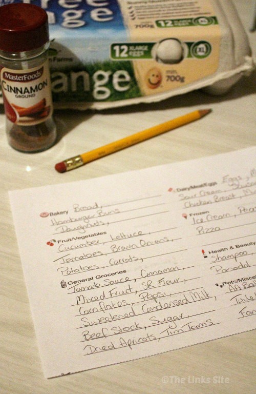 Filled in shopping list on a table with a pencil, a carton of eggs, and a cinnamon spice jar in the background.