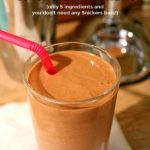 Milkshake in a glass with a pink straw. A milkshake maker can be seen in the background. Text overlay says: Homemade Snickers Milkshake (only 5 ingredients and you don’t need any snickers bars!).