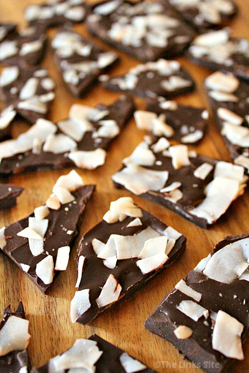 Lots of broken up pieces of chocolate bark topped with coconut flakes scattered on a wooden board.