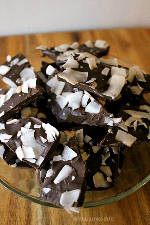 A glass bowl filled with chocolate coconut bark sitting on a wooden chopping board.