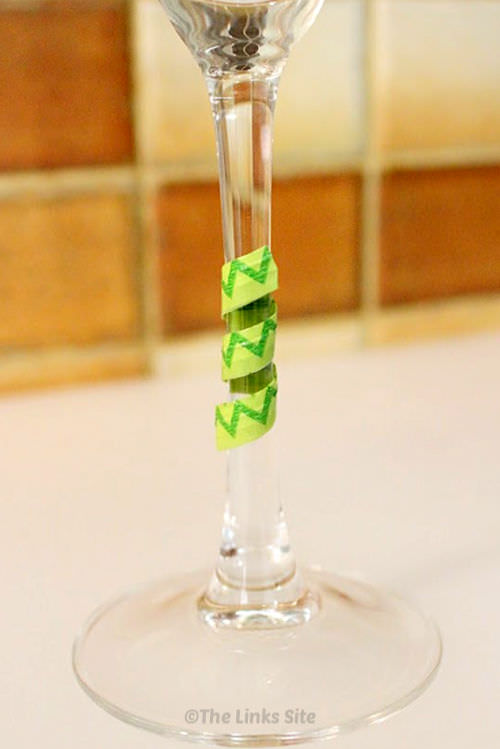 Close up of the stem of a single wine glass. A two tone green wine stem wrap is wrapped around the stem.