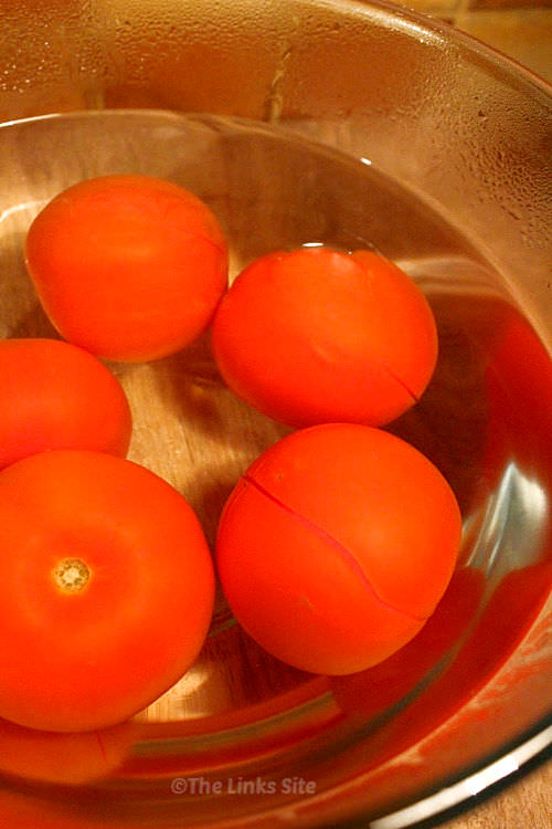 Several tomatoes submerged in a glass dish of boiling water.
