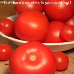 A bowl of ripe red tomatoes of various sizes on a wooden cutting board. A couple of tomatoes are placed on the board in front of the bowl. Text overlay says: How to Peel Tomatoes (so there’s no skins in your cooking!).