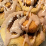 Image is focused on one icing topped cinnamon scroll in the foreground with more scroll in the background.