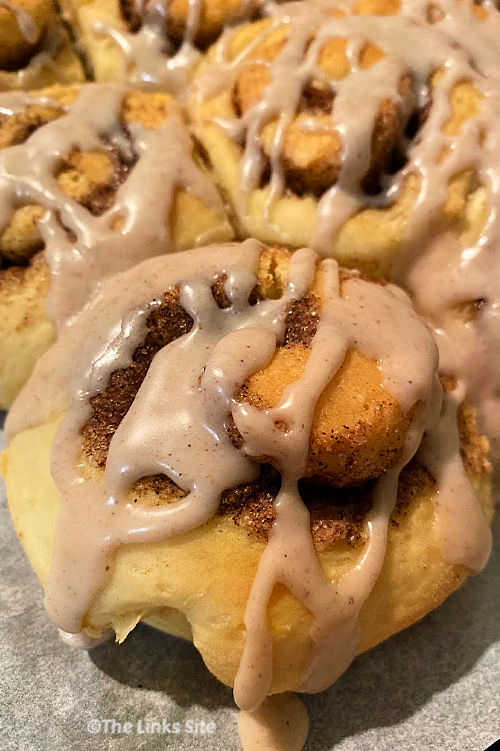 Image is focused on one icing topped cinnamon scroll in the foreground with more scroll in the background.
