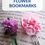 Two flower bookmarks resting on the page of a book. One has a green paperclip with a purple flower and the other has a white paperclip with a pink flower. Text overlay says: Easy to Make Flower Bookmarks.