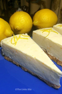 Slices of cheesecake on blue plate. Whole lemons can be seen in the background.