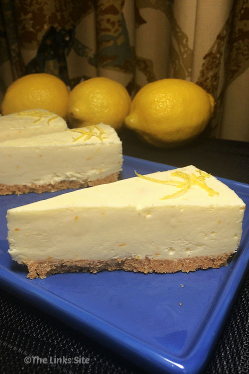 Three slices of cheesecake on a blue plate with whole lemons in the background.