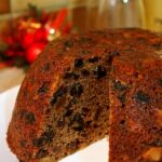 Plum pudding on a white plate, with a slice removed.