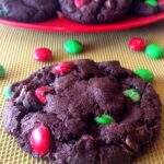 One chocolate cookie on a baking sheet with a plate with more cookies in the background.