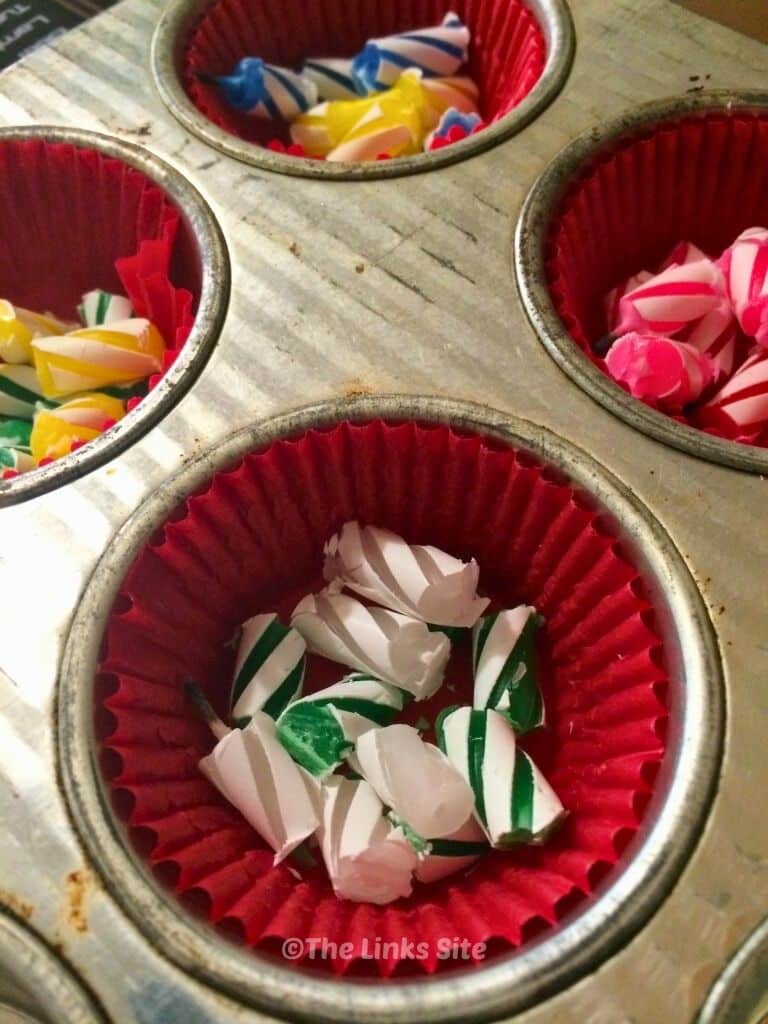 Image shows a cupcake pan with the wells lined with red paper cases. Pieces of broken up birthday candles are lining the bottom of the paper cases.