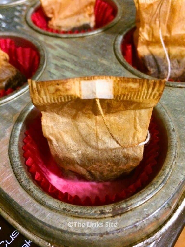 Image shows a cupcake pan with the wells lined with red paper cases. Melted wax and a used teabag is in each paper case.