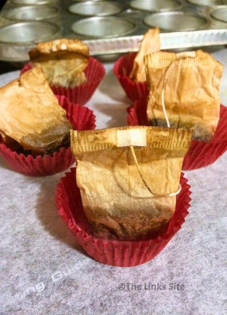 Five firelighters made from cupcake liners, wax, and teabags are cooling on baking paper. A cupcake pan can be seen in the background.