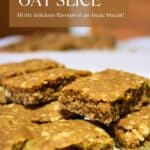 Pieces of Nutty Oat Slice stacked in two layers on baking paper. Text overlay says: Nutty Oat Slice, All the flavours of an Anzac Biscuit!