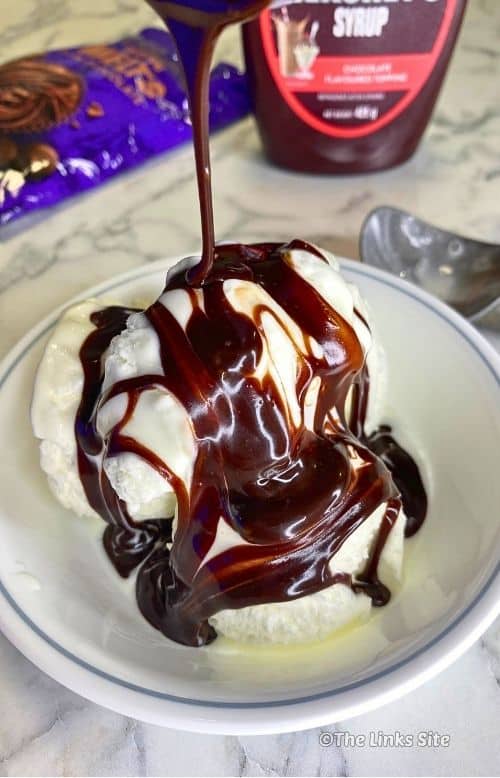 Close-up of vanilla ice cream covered in glossy chocolate sauce, with a ribbon of sauce drizzling down from above.