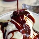 Close-up of glossy hot fudge sauce drizzled over vanilla ice cream, with a thin ribbon of sauce falling from above.