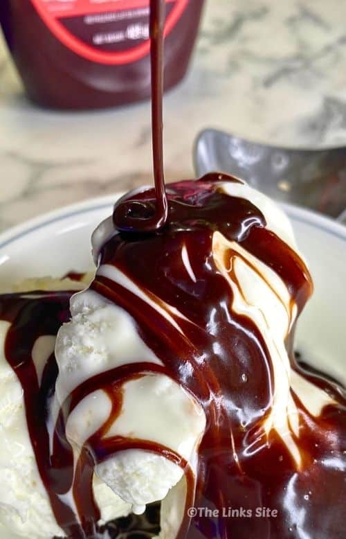 Close-up of glossy hot fudge sauce drizzled over vanilla ice cream, with a thin ribbon of sauce falling from above.